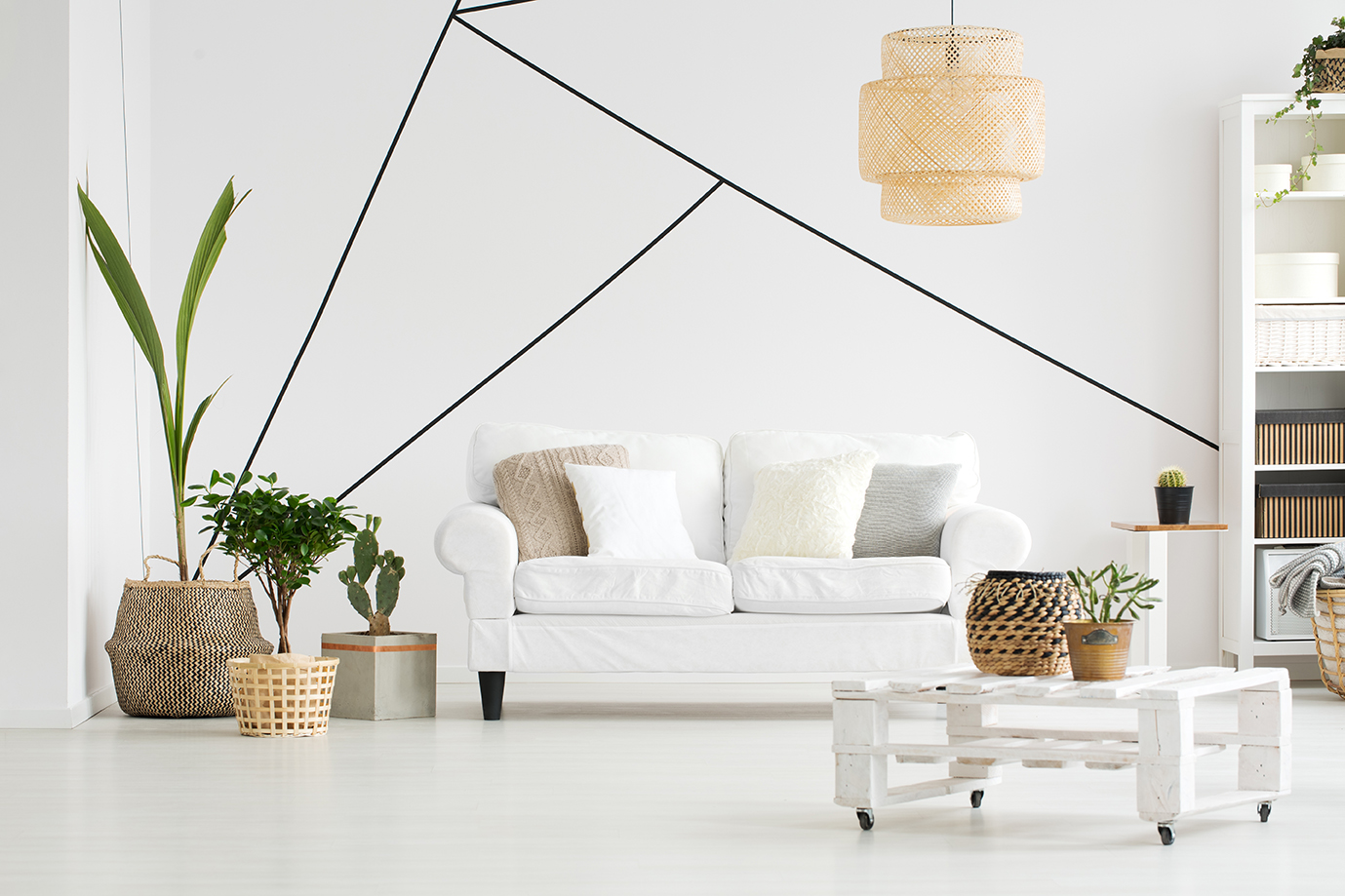 Bright, white living room furnished with a white couch, plants, and coffee table in front of a minimalist geometric wall design.